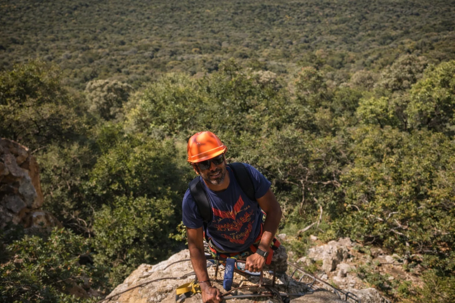 Climber reaching the ridge in an orange helmet with the Magaliesberg bush below.