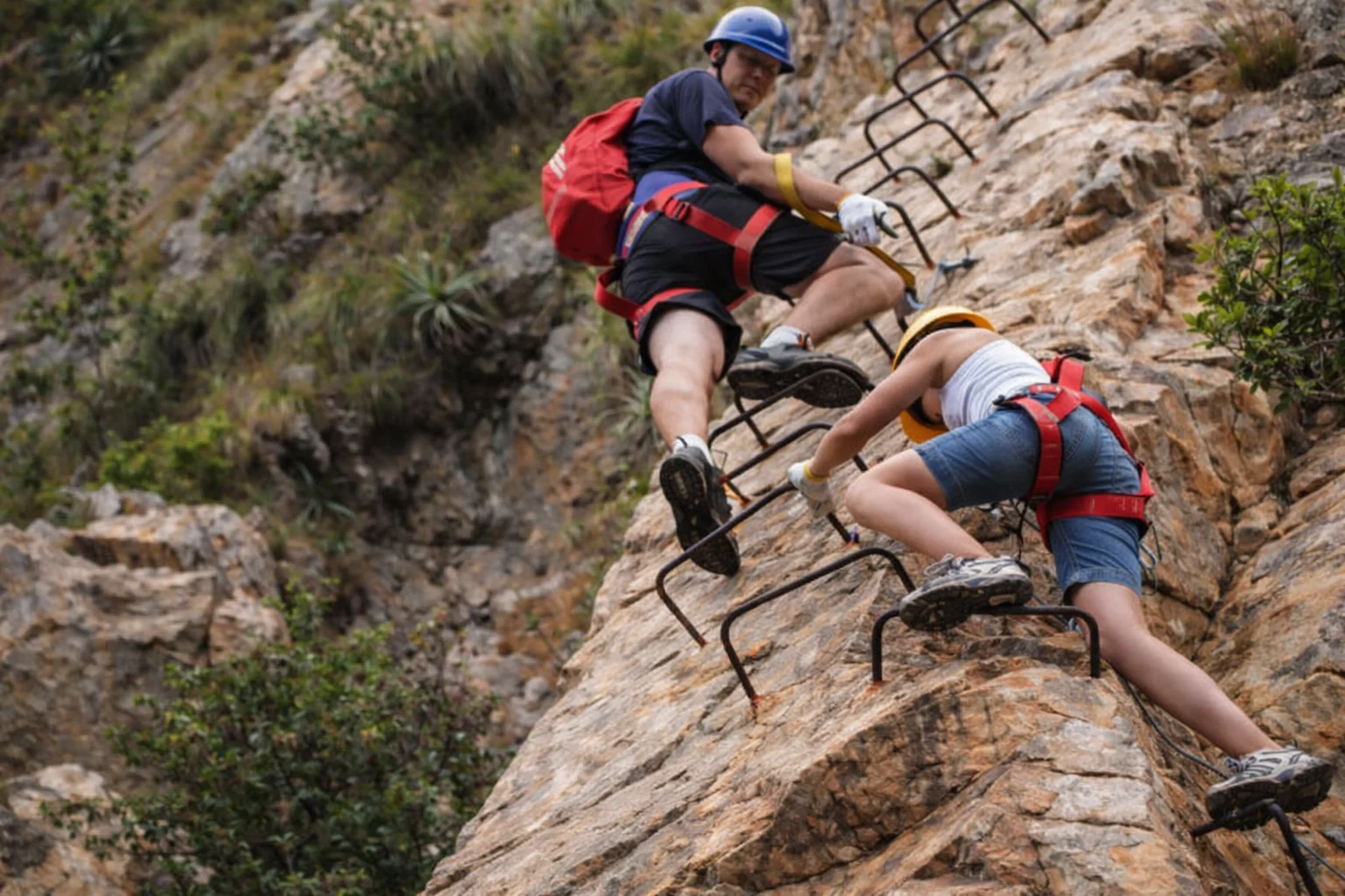 Two climbers ascending iron rungs bolted into a Magaliesberg cliff on the Shelter Rock Via Ferrata.